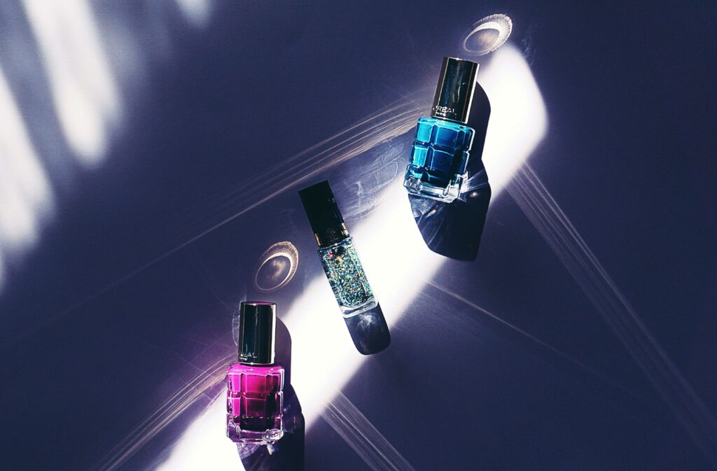 À propos A close-up view of colorful nail polish bottles on a dark surface with striking light patterns.