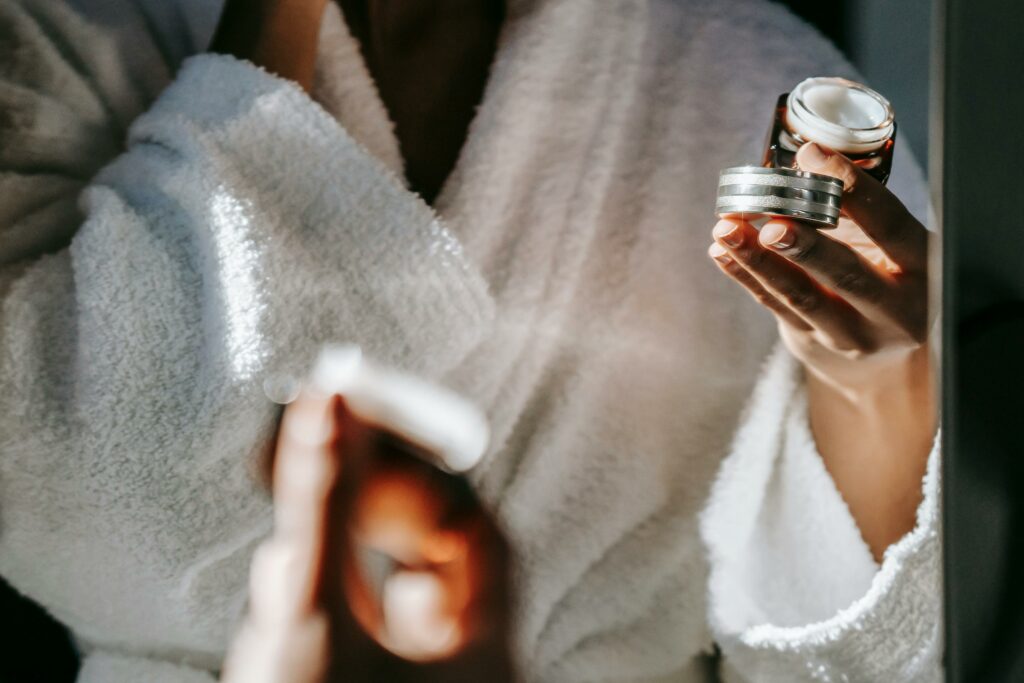 À propos Woman in bathrobe applying skincare cream for a calm morning routine.